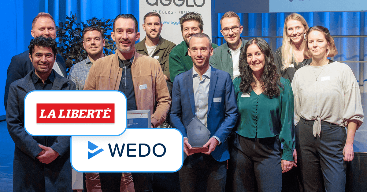 A group of smiling professionals standing on a stage with an AGGLO Fribourg–Freiburg banner behind them, two in front holding awards and others gathered closely, overlaid with the “La Liberté” logo and the WEDO logo